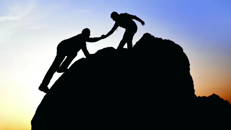 Being in a person’s bosom can also mean that a person or thing is embraced or cherished. Silhouette of a person helping another person climb a boulder.