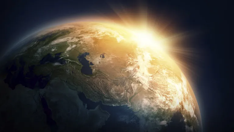 A sun burst shining around the side of the earth from space.