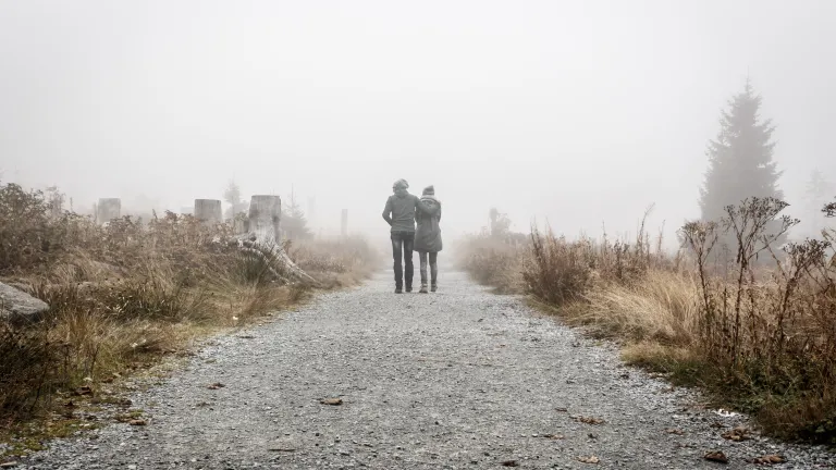 Two people walking together on a gravel path.
