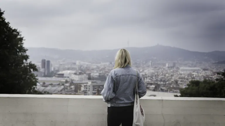 How often do we lie to ourselves and not even know it? A woman standing by a brick wall looking out over city buildings.
