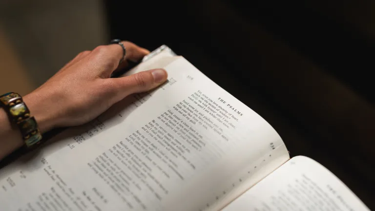 The Bible is a collection of books which were written by many authors over thousands of years under the divine inspiration of God. A woman holding a Bible opened to the Psalms.