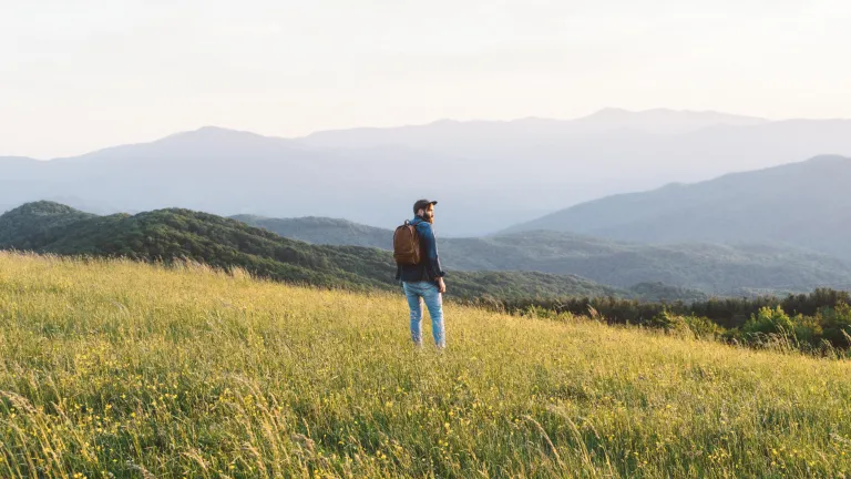 A man hiking in field with mountains in the background.