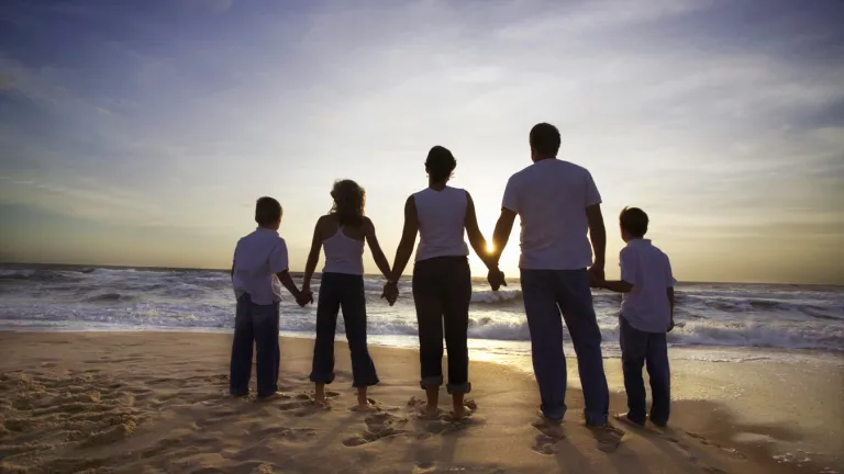 A family holding hands looking at the ocean waves and the sun setting.
