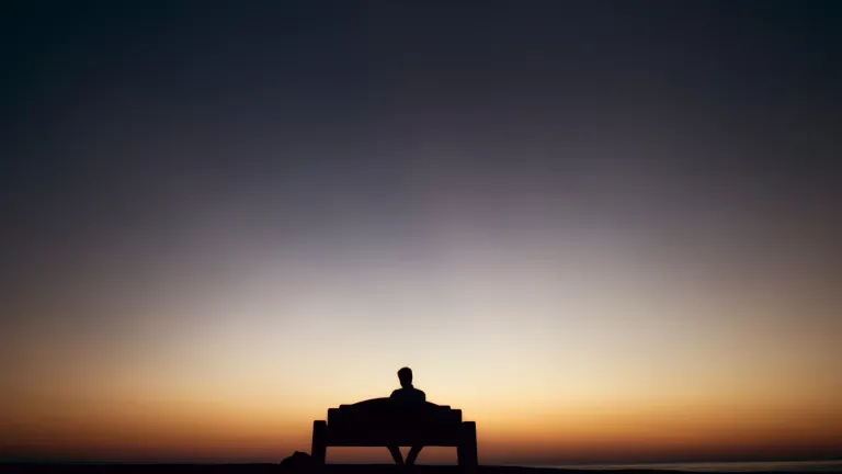 While we may want to vote for the person that most reflects our godly beliefs, there is no earthly person that can fulfill the true need. A person sitting on a bench with the sun setting.