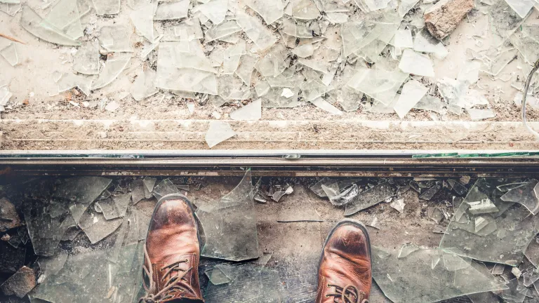 A person looking down at broken window glass.