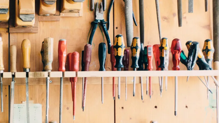 A workbench wall with many types of screwdrivers hanging.
