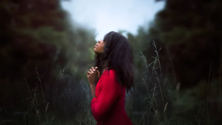 A young woman praying in a field.