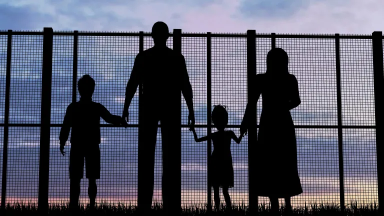 A family of four looking through a tall fence.