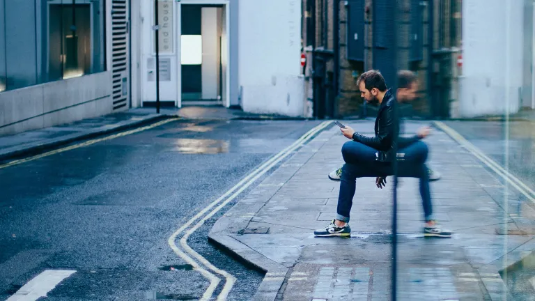 Various websites kept us busy enough, but then the Internet moved to our phones. Social media, movies, TV and games could now be accessed anytime and anywhere. We forgot how to deal with boredom—how to take time to dwell on our thoughts. A man sitting by a building looking at his phone.