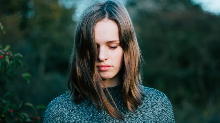 A young woman holding her head down facing the ground.