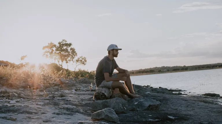A man sitting on a log by a lake.