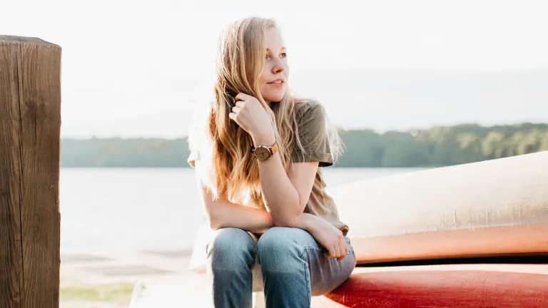 A young woman sitting on the edge of kayak that is on the shore.