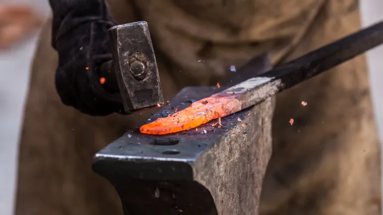 Close-up photo of a hammer striking a heated piece of metal.