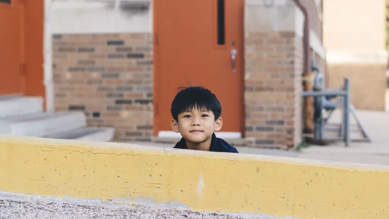 A little boy hiding behind a yellow wall.