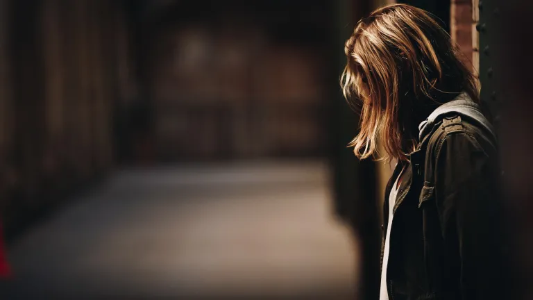 Pray that God will give us a completely different heart—a spirit of peace, which is opposite of hate. A young woman with her back against a wall with her head looking down.