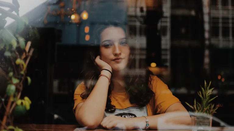 A young woman sitting with her arms on a counter looking through a window.