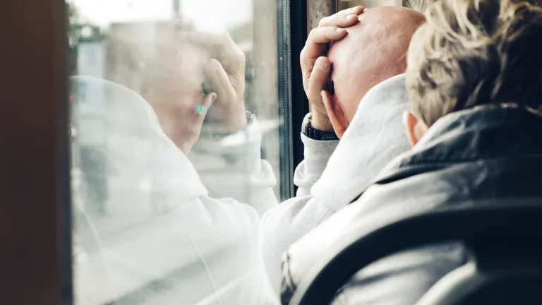 A man leaning his head against a train window.