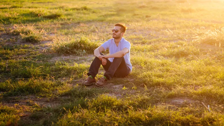 Joy has a wonderful emotional range, from outrageously wacky to light-hearted puns to calm smiles, thanks to our brilliant, creative designer.  A man sitting in a field with the sun rays shinning.
