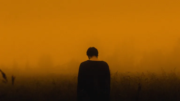 A person with their head down. The sky is red.