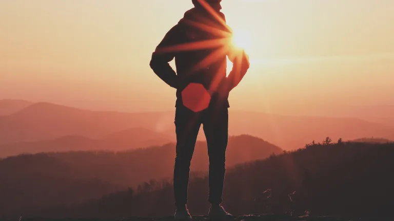 A person standing on the rock with the sun behind them.