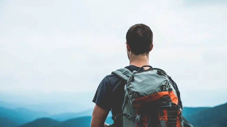 A guy wearing a backpack at the top of a hill.