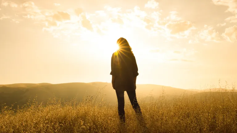 How can we know if we have God’s Holy Spirit? A woman standing in front of sun rays in an open field.