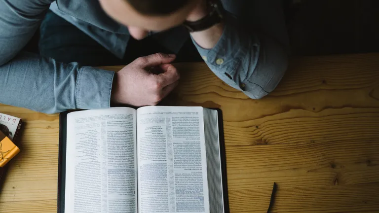 A man reading a Bible on a table.