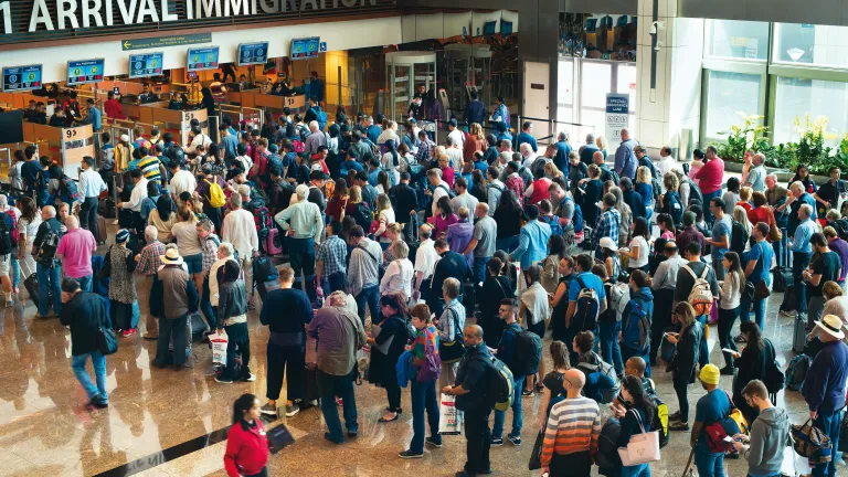 Through modern transportation, our technologically advanced world sets the stage for pandemics to spread with astounding speed. Airport travelers standing in line to go through immigration customs.