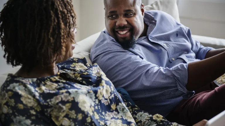 An important way to deepen a loving friendship with your spouse is to take the time to have fun together. It’s the gift that keeps on giving. People love to laugh, a wonderful activity that’s healthy for us in our marriages. A couple sitting together on a couch laughing.