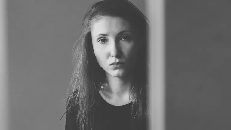 A young woman looking from behind an edge of a wall.