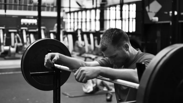 A man resting his arms on a weight lifting bar.