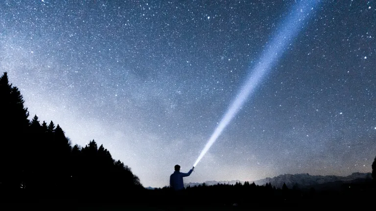 Is there life in outer space? A person pointing a flashlight beam up into the night sky.