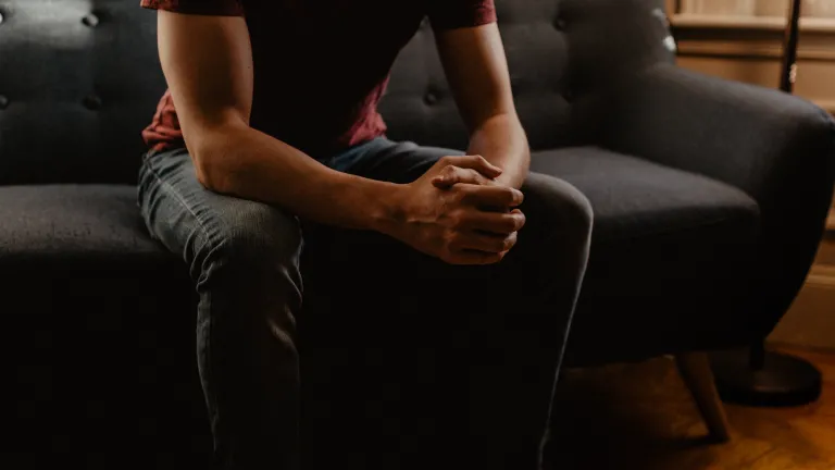 A young man sitting on a couch clasping his hands.