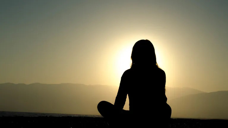 A woman sitting on the ground watch the setting sun.