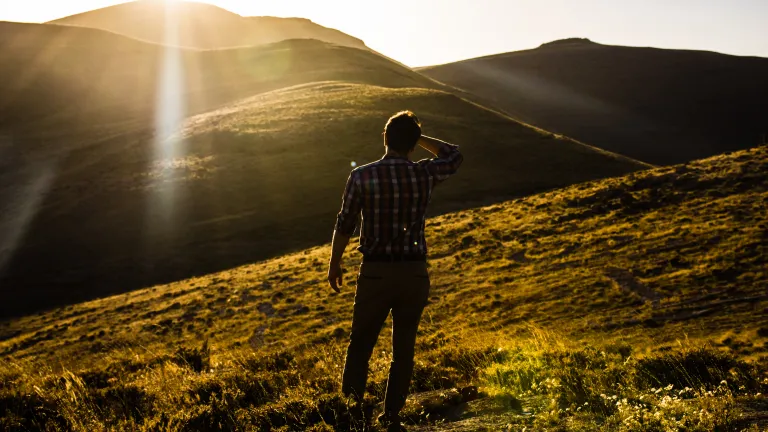 A man looking out over a vista of hills with the sun in his eyes.