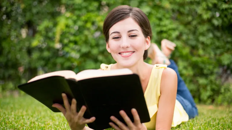 A woman reading a Bible while laying on a grassy field.