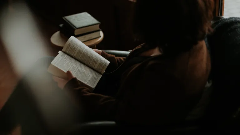 A sitting in a chair reading a Bible.