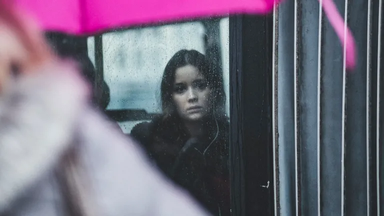 A woman looking out a window when it is raining.
