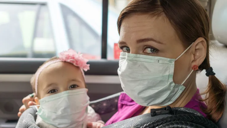 A woman and small child wearing face masks sitting in a car.