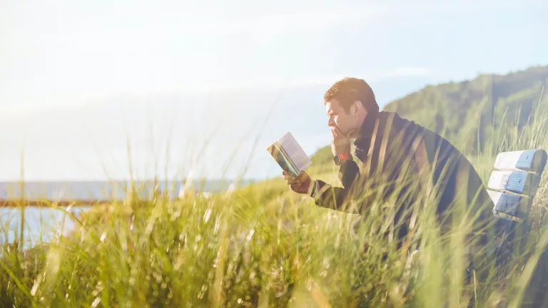 Man sitting in field studying Bible alone.