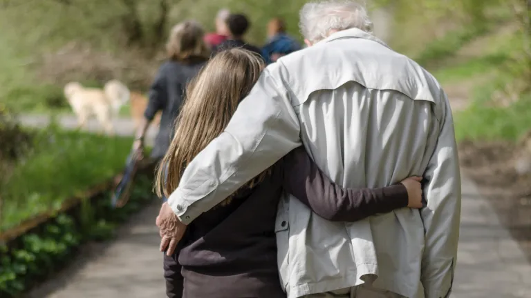 As seniors go on toward perfection, they have the opportunity to set a righteous example as they serve and give in their families, communities and the Church. Photo of a young girl on the left and old man on the right, walking along a paved trail in a park, each with an arm around the other.
