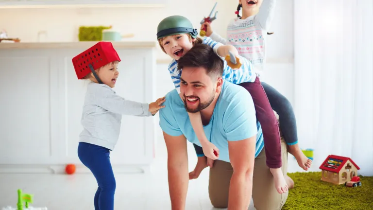 Child studies show that rough-and-tumble play with dad helps children develop social and emotional experiences that prepare them for school. A dad playing with his kids.
