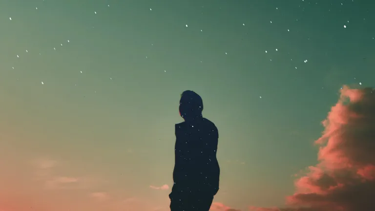 What Makes You a Christian? Silhouetted person against a dramatic, colorful sunset sky, with the person's silhouette filled with a different background, of a starry sky.
