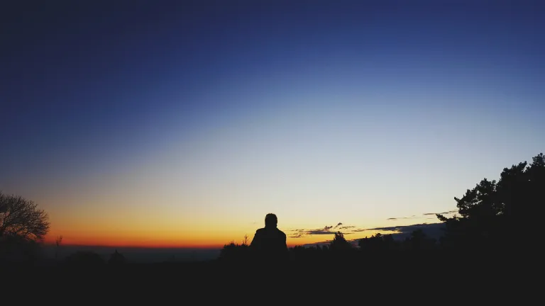 God has been working out a marvelous plan. A long, thoughtful and loving story has been unfolding right alongside the pain of human drama. A person sitting at the top of hill looking at the expanse of the night sky.