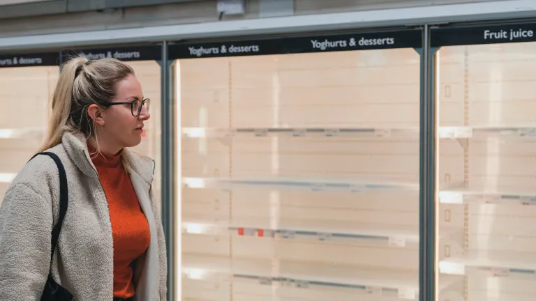 A woman looking at empty shelves inside a grocery store.