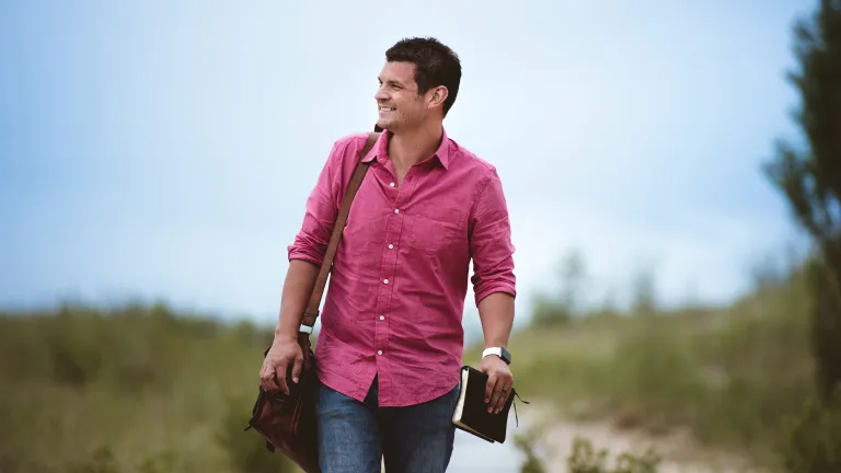 a smiling man carries a Bible as he walks