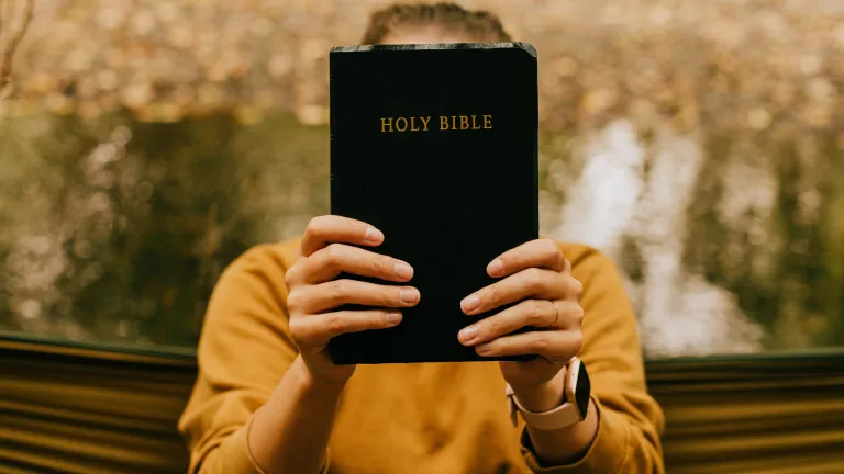 A woman holding a Bible in front of her face.