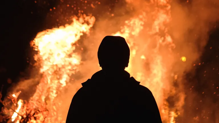 God does not harbor evil thoughts of taking enjoyment in the torment of immortal souls. the silhouette of a person standing in front of leaping flames of fire