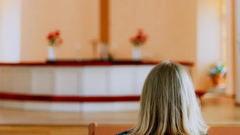 A woman sitting in church looking toward the alter and cross.