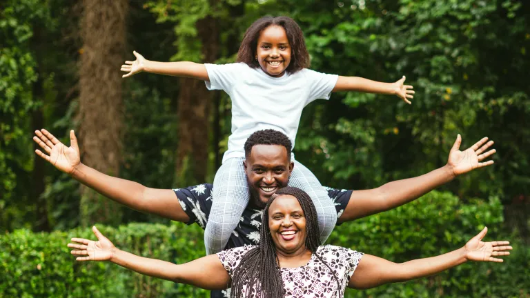 a man, woman, and child standing outdoors with outstretched arms and smiles